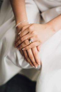 A bridge clasps her hands together upon her wedding dress, showing her wedding band
